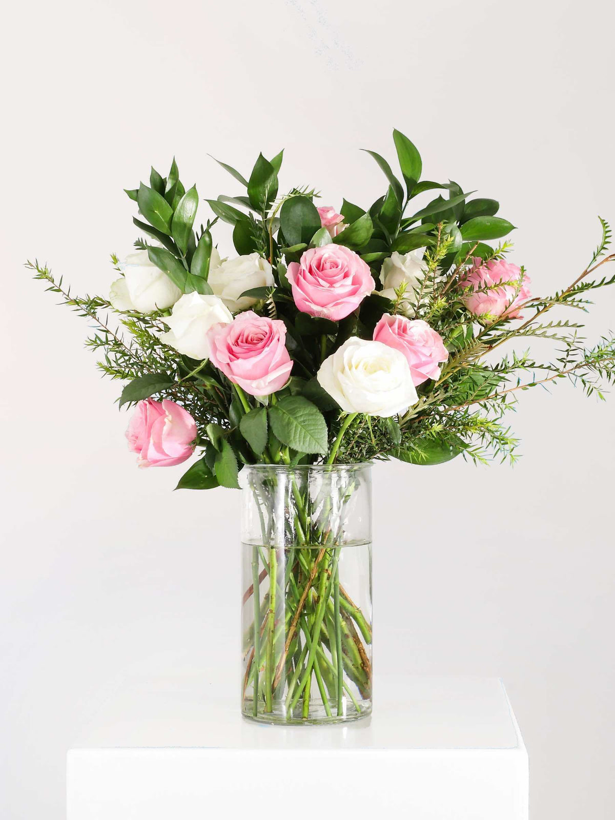 Vase of pastel pink and white roses with lush greenery, elegantly arranged to convey calm and beauty, perfect for gifting or home decor.