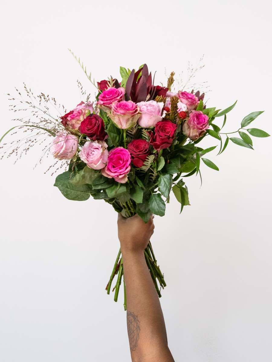 Bouquet of pink and red roses with greenery for Valentine's Day, symbolizing love and romance, held by a hand on a white background.