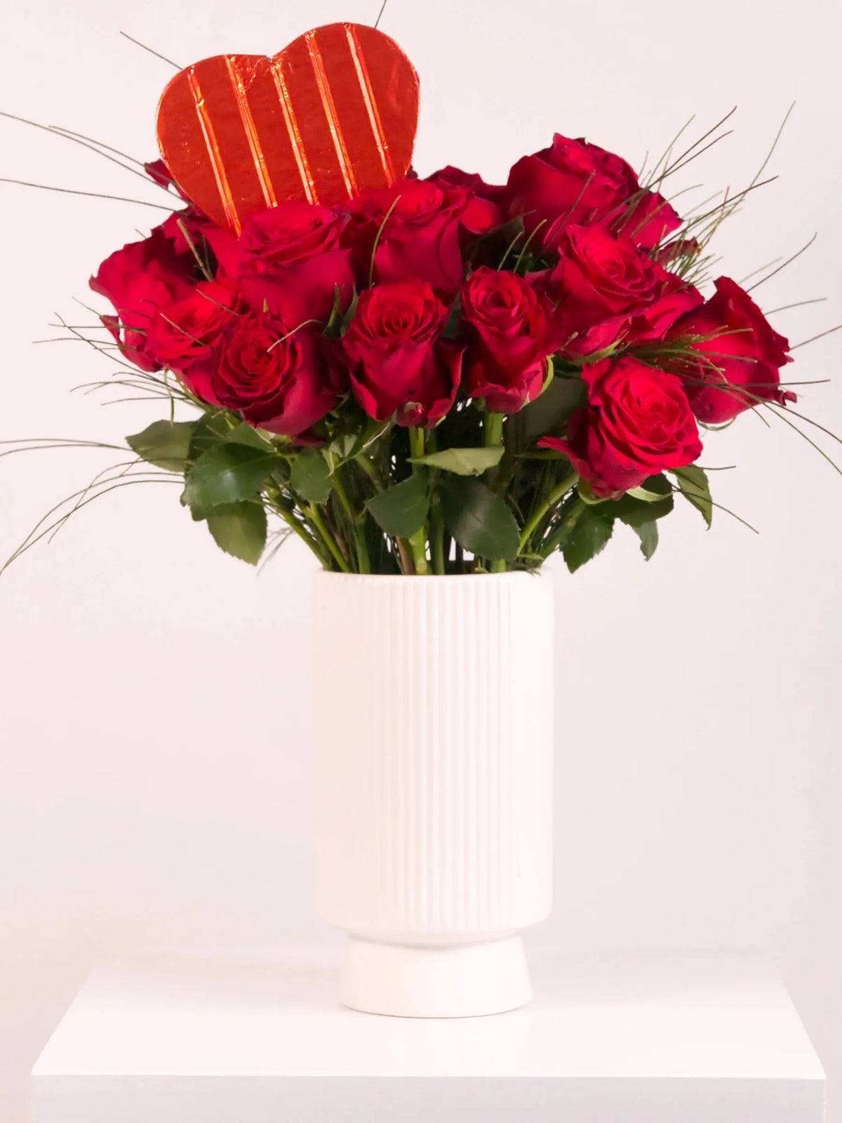 Bouquet of red roses in a white vase with a heart-shaped object on a white background