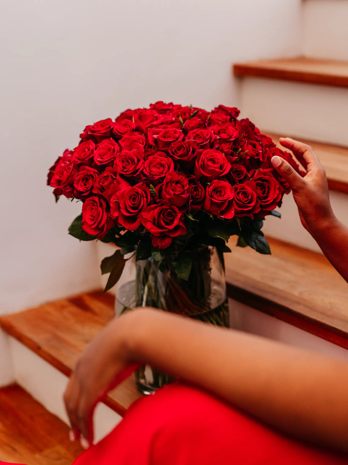 Bouquet of red roses in a vase held by a person on wooden stairs.