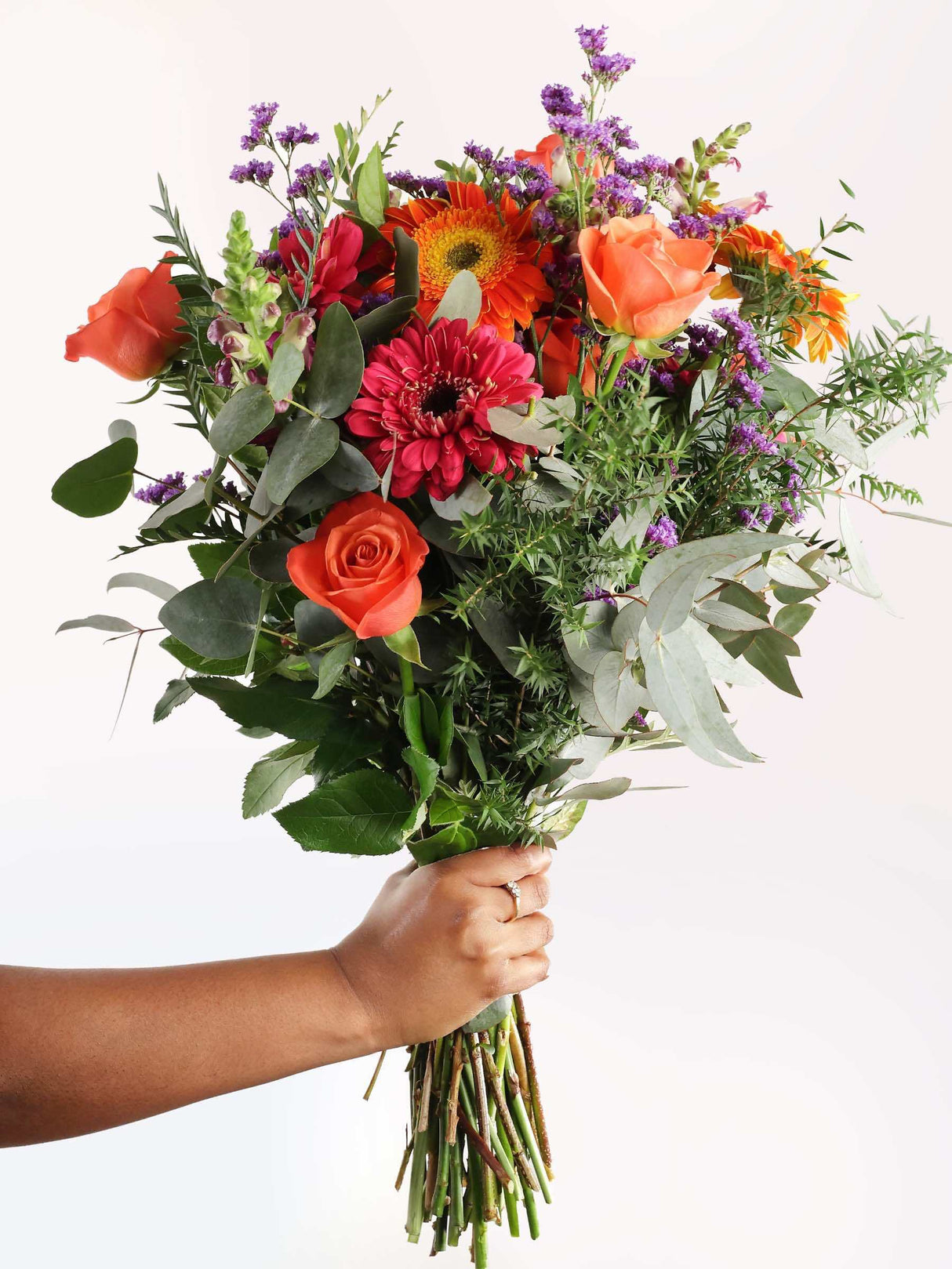 A hand holding a beautiful bouquet of flowers with a variety of colors including pink, orange, and purple, arranged elegantly.