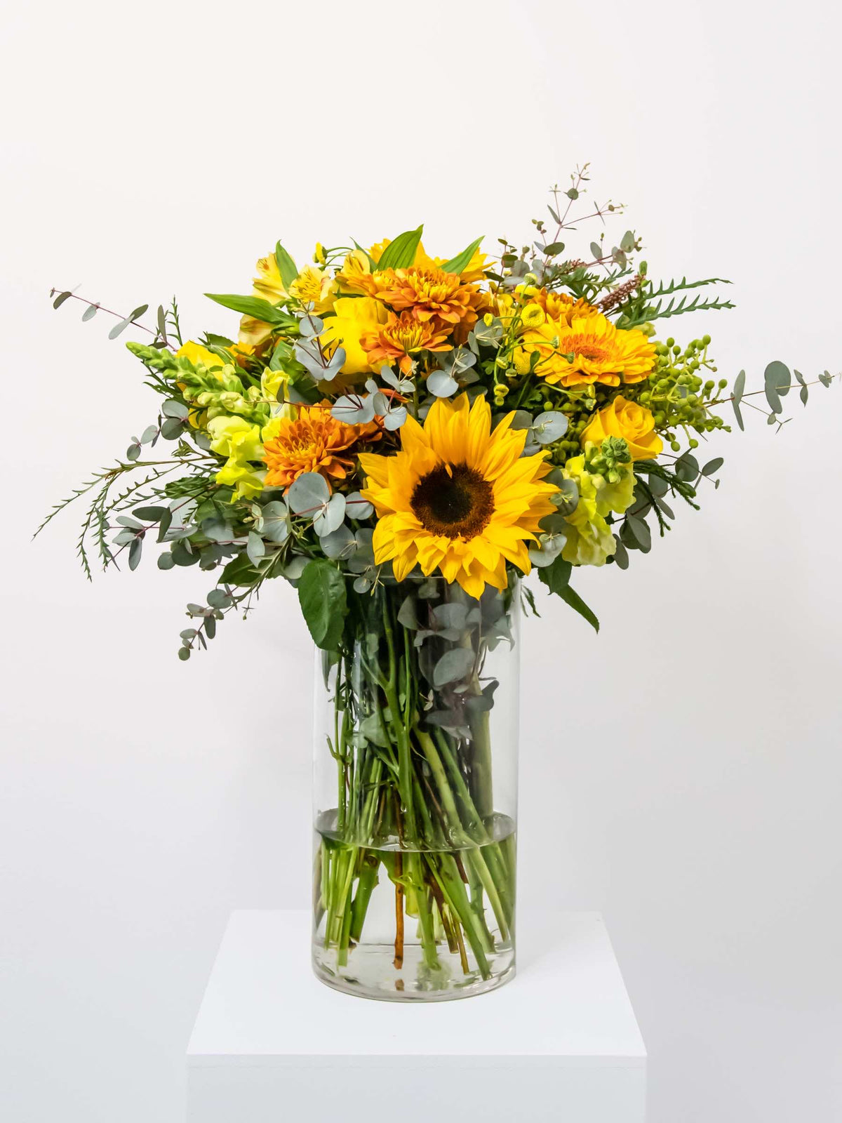 Bright and cheerful bouquet in a clear vase featuring sunflowers and mixed yellow flowers, perfect for gifting to family and friends.