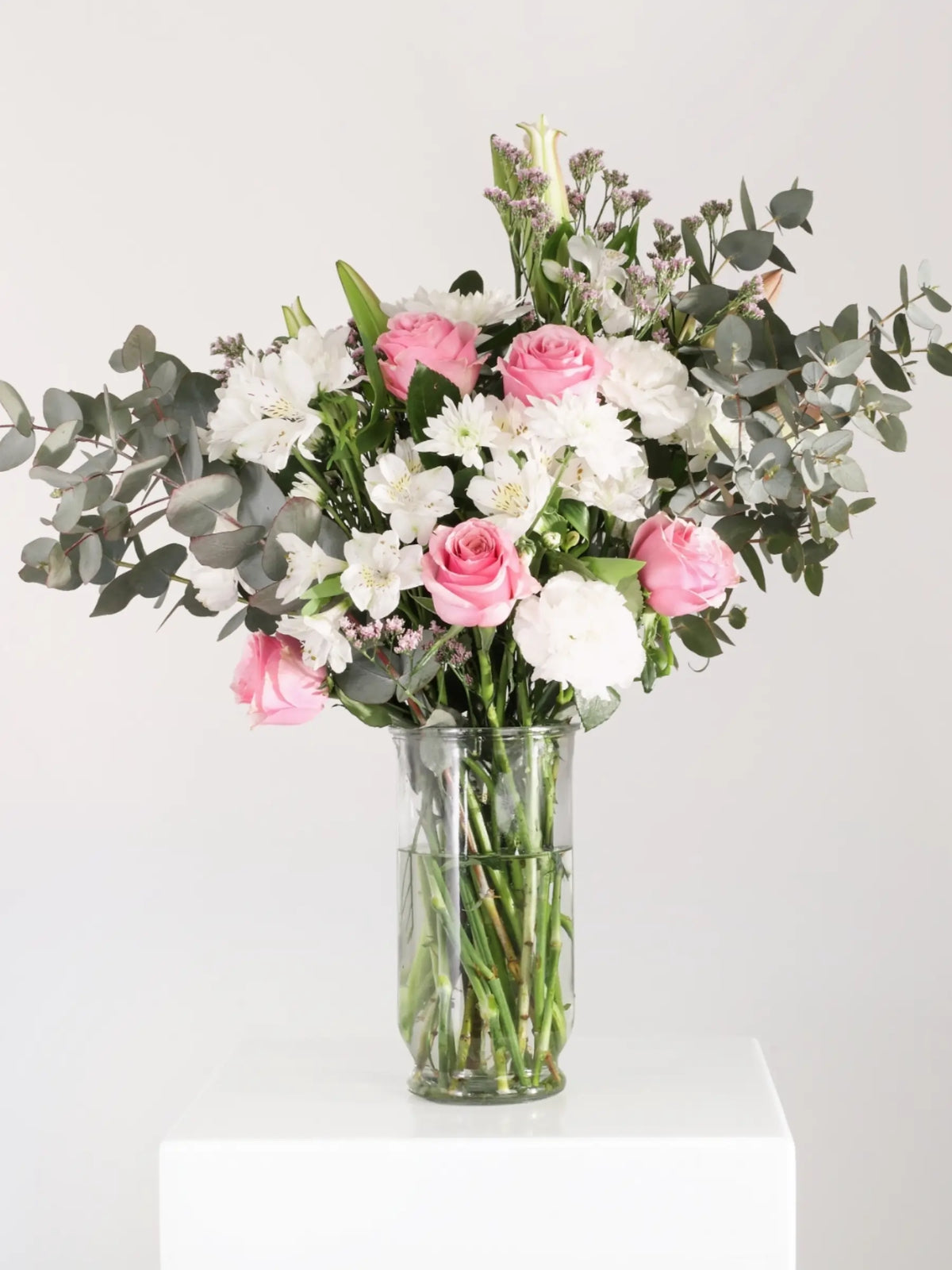 Fresh pink and white flower arrangement with pink roses, white alstroemeria, white carnations and eucalyptus in clear glass vase - classic romantic bouquet