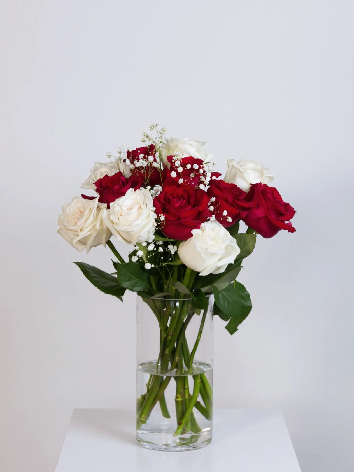 Red and white rose bouquet with baby's breath in a glass vase