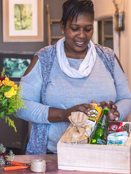 Local florist curating a Florist's Choice Gift Box filled with snacks and goodies, supporting South African local businesses.