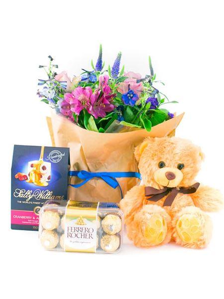 Newborn boy gift set with blue and purple flowers, teddy bear, Sally Williams nougat, and Ferrero Rocher chocolates.