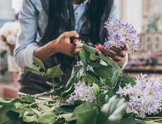 Person arranging flowers with a focus on greenery and purple flowers.