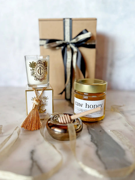 Jar of raw honey with a honey dipper, candle, and gift box on a marble surface.