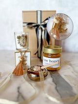 Honey jar, candle, and decorative items on a marble surface with a gift box in the background.
