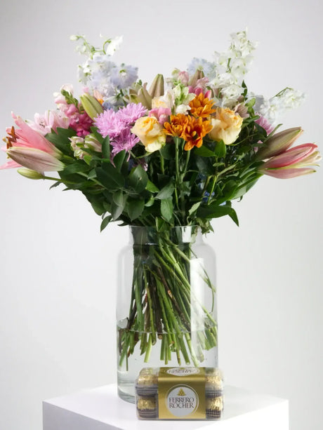 Vase filled with colorful flowers and a box of Ferrero Rocher chocolates, perfect for sending joy.