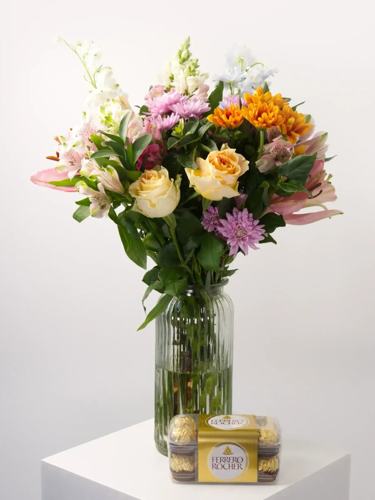 Bright floral bouquet with pink snapdragons, orange roses, and Ferrero Rocher chocolates in a vase.