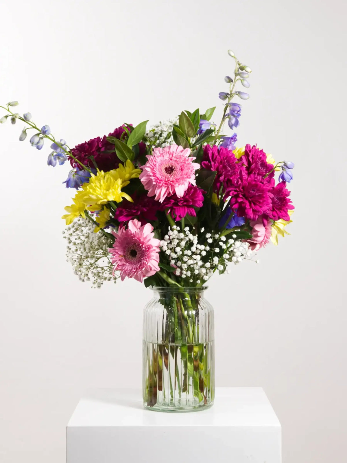 A cheerful bouquet with Gerbera daisies, chrysanthemum, delphinium and gyp in a glass vase or wrapped in kraft paper perfect for Teacher's Day or a pick me up for a good friend.