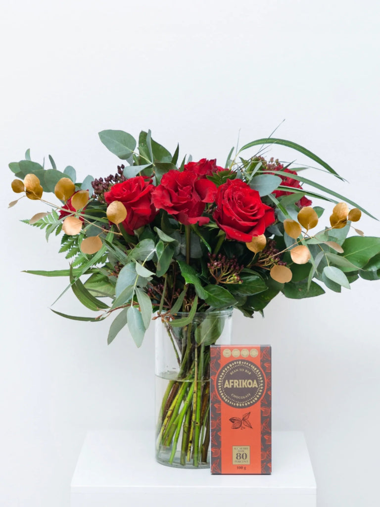 Bouquet of red roses and greenery with a box of Afrikoa on a white background.