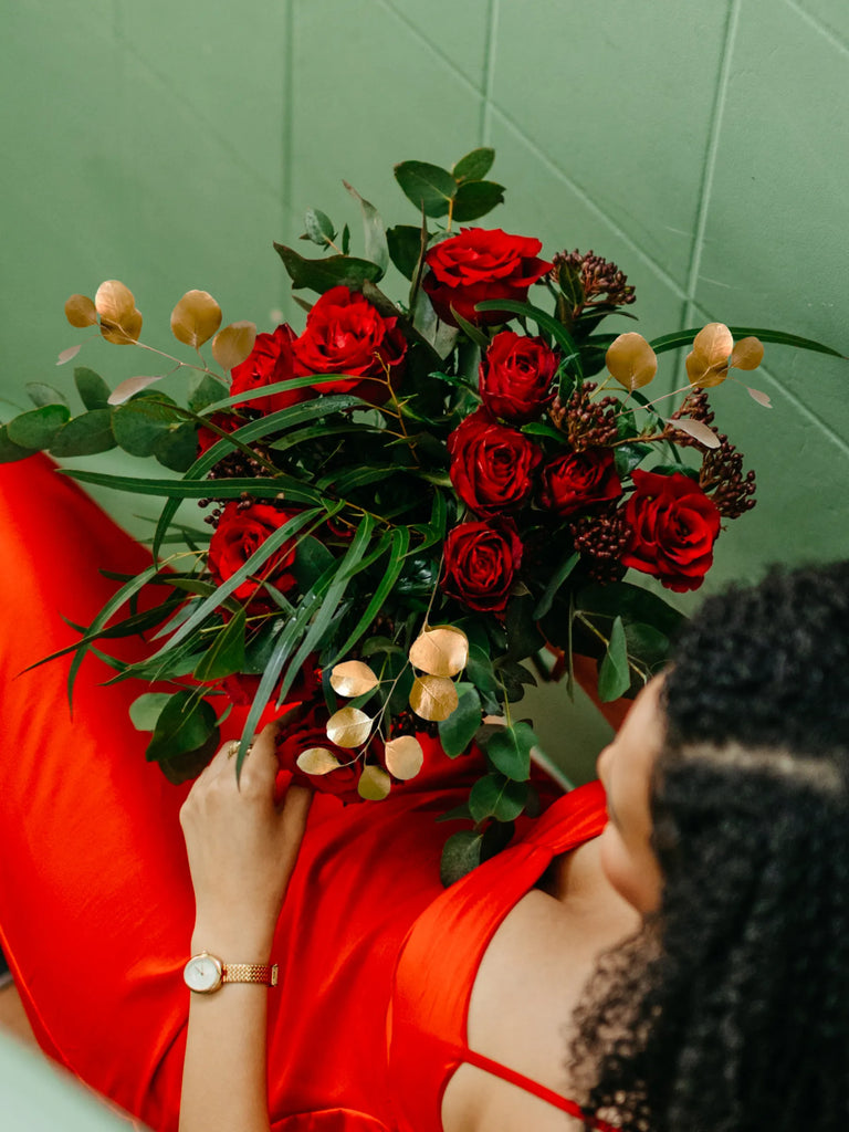 Woman in a red dress holding a bouquet of red roses against a green wall.
