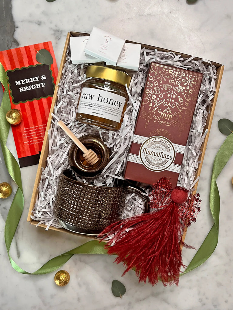 Gift box with raw honey, a candle, and a card on a marble surface