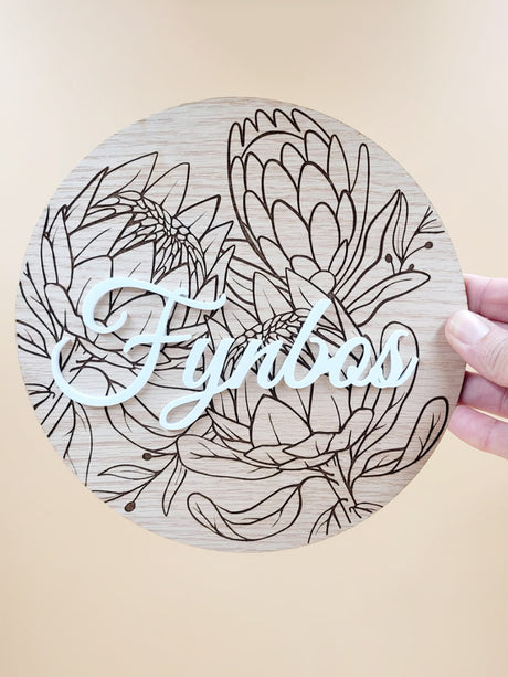 Laser-cut personalised floral wooden plaque held in hand, featuring intricate engraved floral design with 'Fynbos' text.