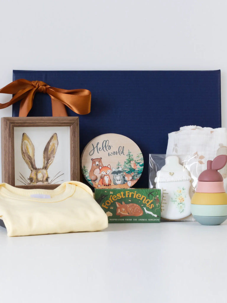 Forest Friends Baby Rabbit Gift Set – a woodland-themed baby gift box featuring a soft muslin swaddle, a pear silicone teether, hand-painted rabbit watercolour in a wooden frame, twelve wooden monthly milestone discs, baby bottle-shaped shortbread cookie, forest animal affirmation cards, and a soft cotton babygrow vest, arranged beautifully in a neutral-toned gift box with ribbon