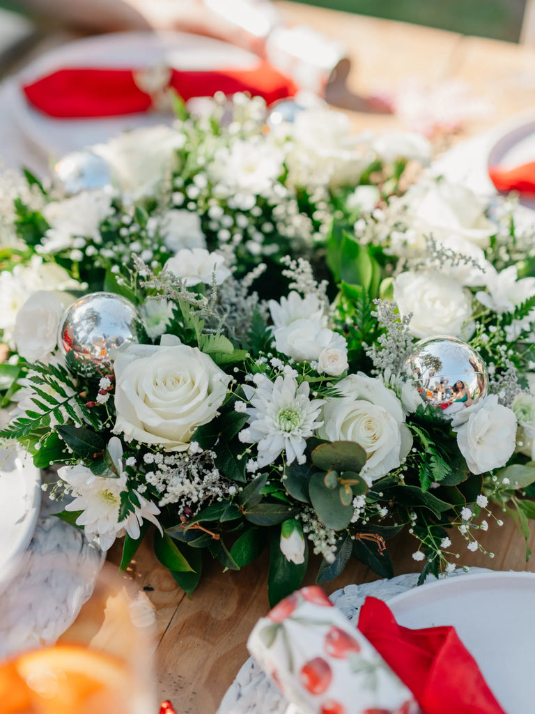 Decorative floral arrangement with white flowers and silver ornaments on a table.