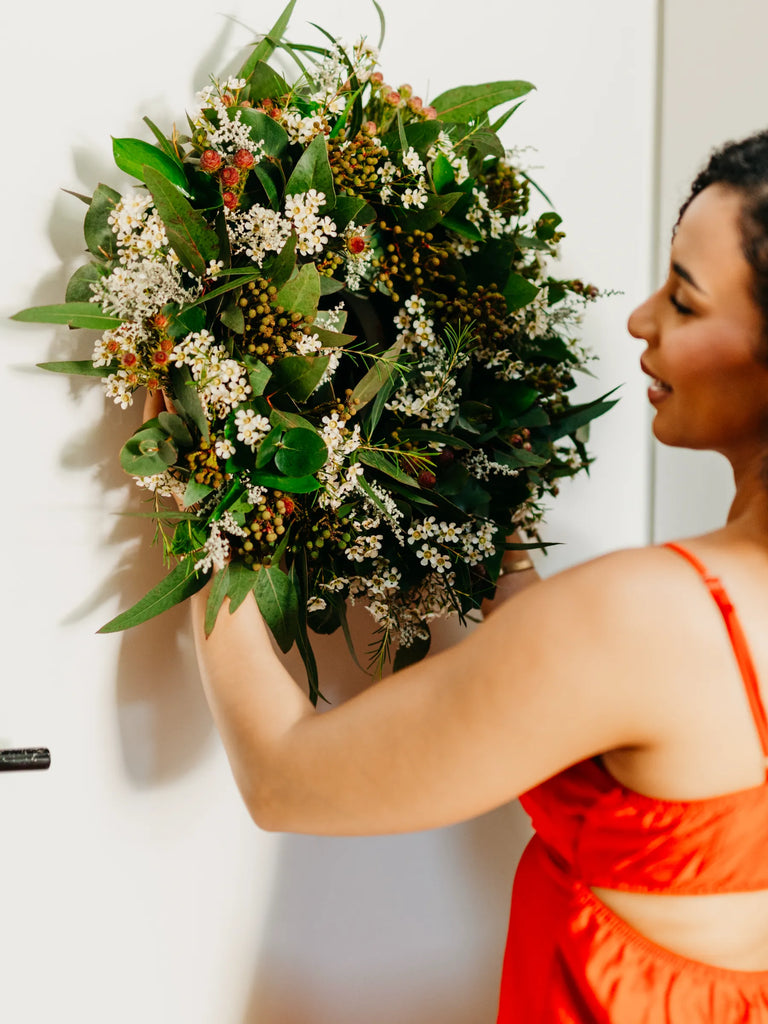 Large rustic Christmas wreath featuring white blooms, eucalyptus, mixed greenery and berries held to show scale - natural organic festive door wreath
