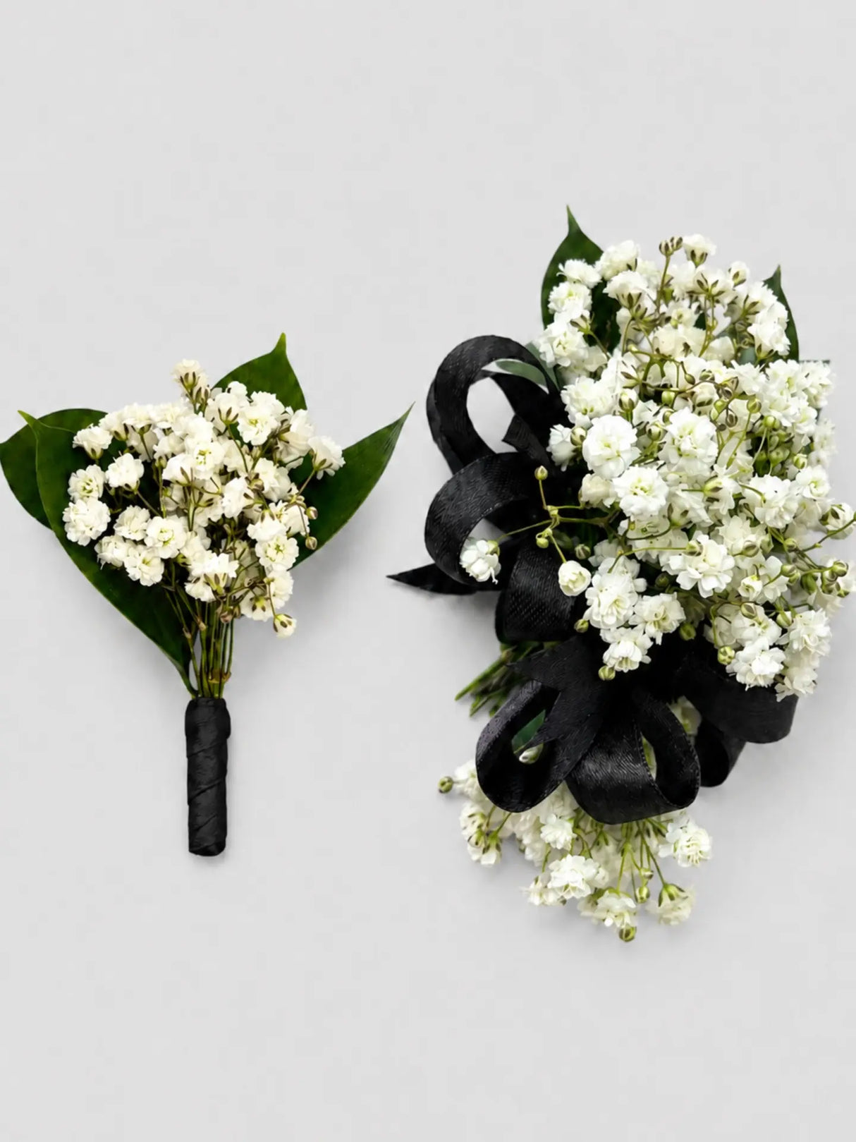 Two floral arrangements with white flowers and black ribbons on a light gray background