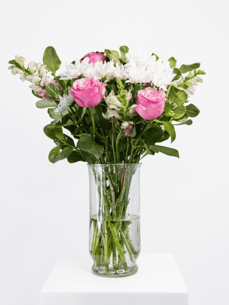 Pink, fuchsia, and white bouquet with lush greenery in a glass vase, offering a fresh and playful floral arrangement.