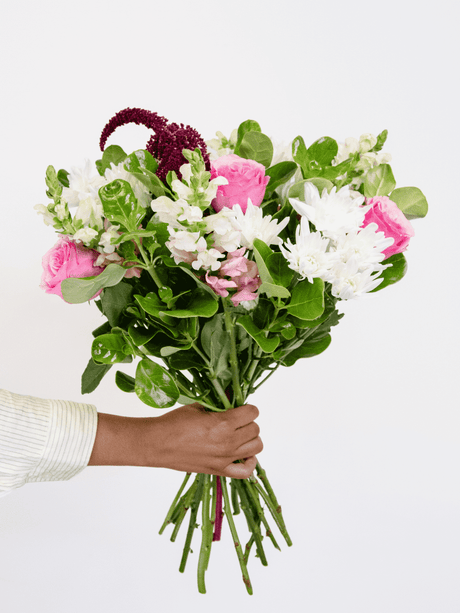 Hand holding a pink and white bouquet with greenery, featuring fresh garden blooms, ideal for gifts or special occasions.