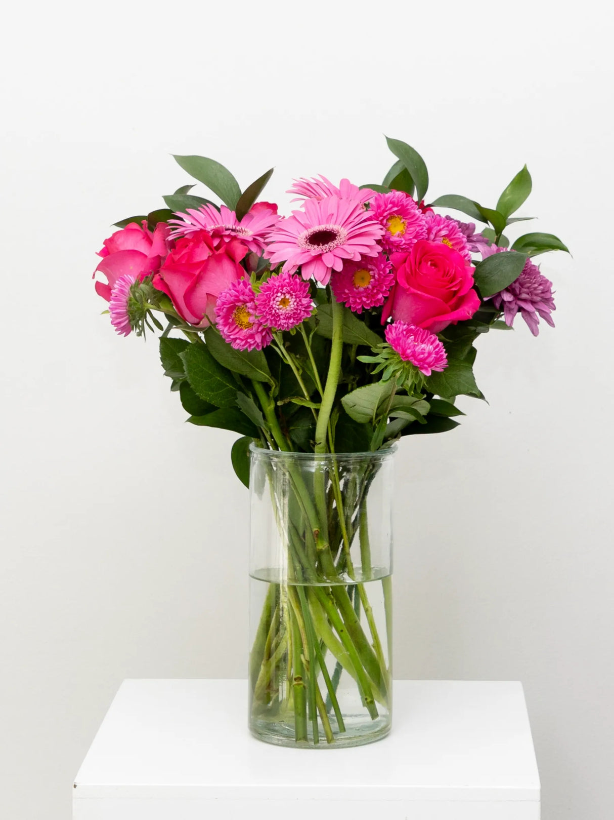 Bouquet of pink flowers in a clear vase on a white surface with a white background