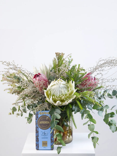 Bouquet of proteas and fynbos with a box of chocolates on a white surface