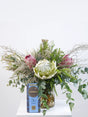 Bouquet of proteas and fynbos with a box of chocolates on a white surface