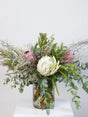 Floral arrangement with protea and eucalyptus in a clear vase on a white surface.