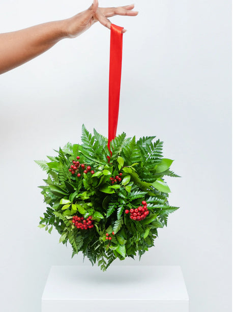 Fresh Christmas kissing ball with evergreen foliage, red berries and red ribbon - traditional hanging holiday decoration