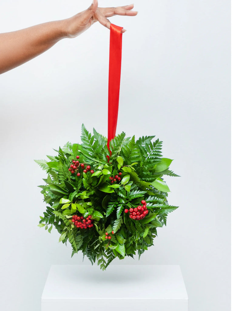 Fresh Christmas kissing ball with evergreen foliage, red berries and red ribbon - traditional hanging holiday decoration