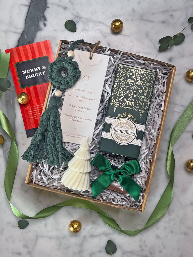Gift box with decorative items including a green crocheted ornament, white candy, and a red book on a marble surface.