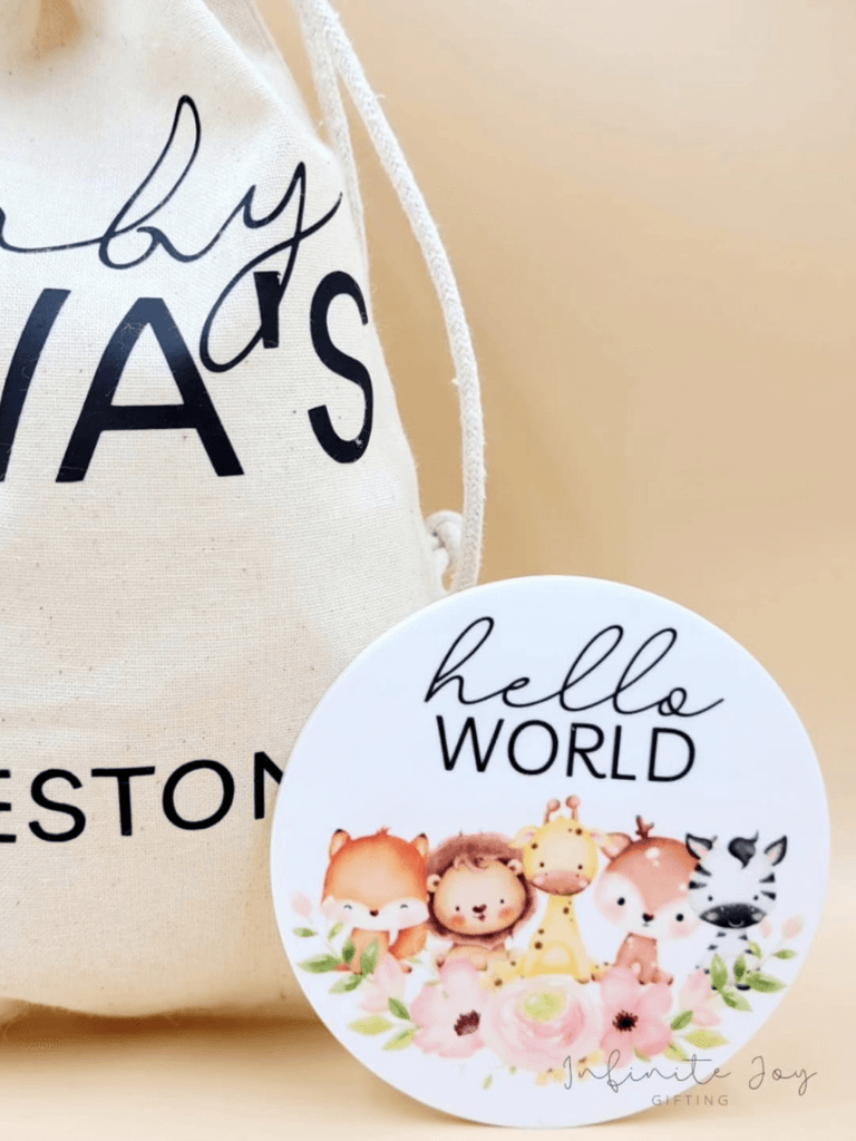 Close up of "Hello World" baby animal printed disc alongside personalised cotton drawstring bag. 
