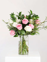 Vase of pastel pink and white roses with lush greenery, elegantly arranged to convey calm and beauty, perfect for gifting or home decor.