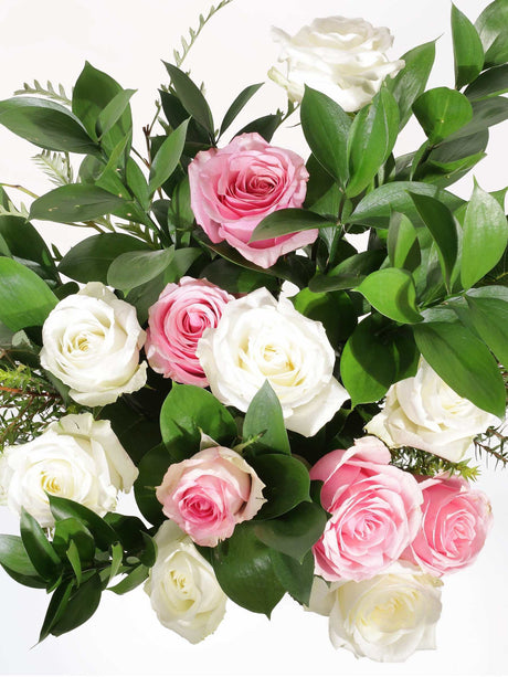 Pink and white pastel roses with lush green leaves, elegantly arranged to enhance any space with beauty and warmth.