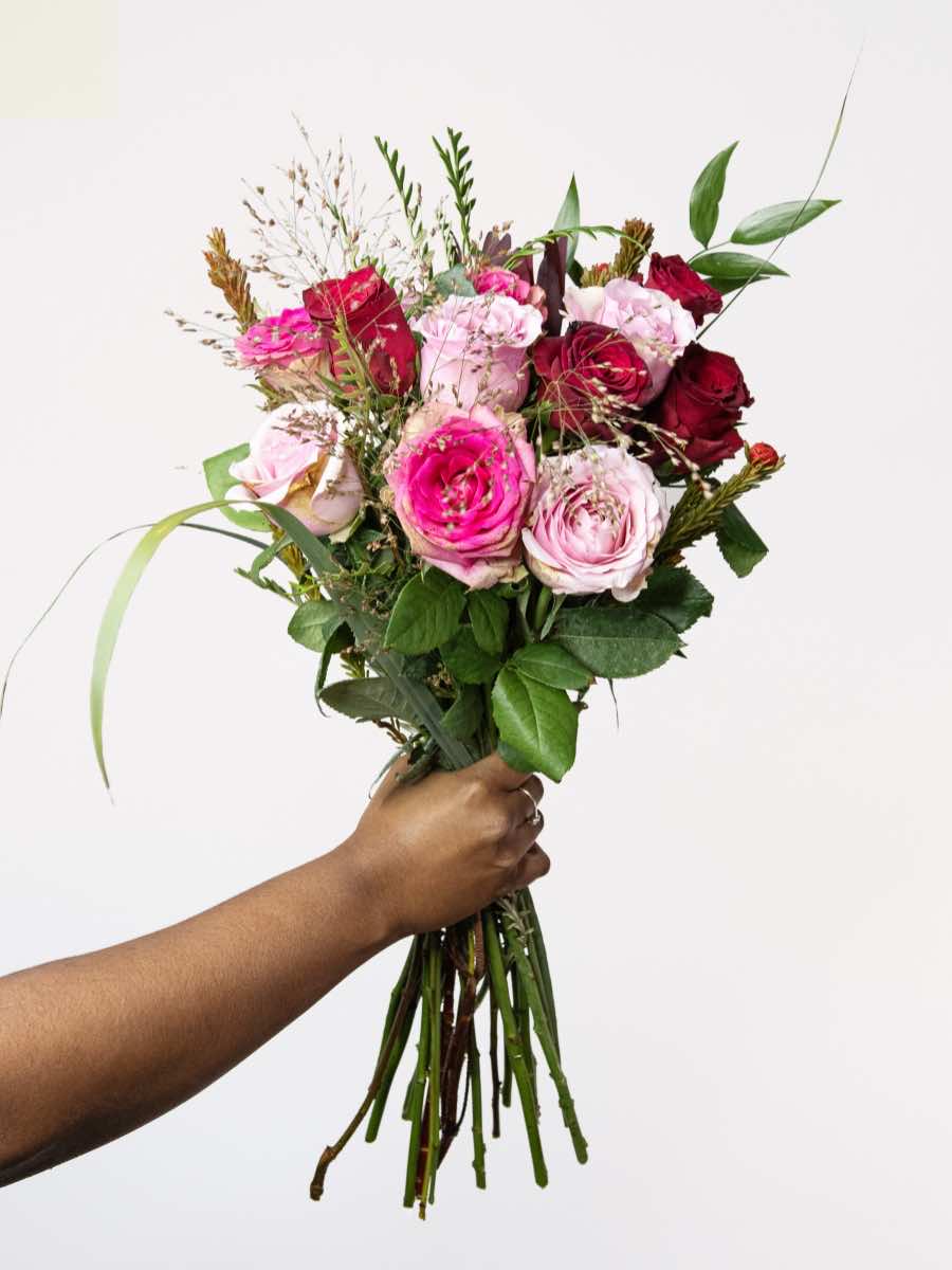 Hand holding a bouquet of freshly cut pink and red roses with greenery, perfect as a romantic Valentine's Day gift.
