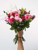 Hand holding a bouquet of pink and red roses with greenery, perfect for Valentine's Day gifts, symbolizing love and romance.