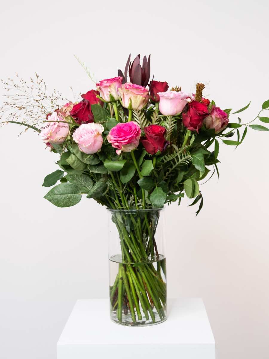 Valentine's Day bouquet with pink and red roses, contrasting greenery in glass vase, ideal romantic gift for love and passion.
