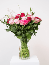 Delightful bouquet of freshly cut pink and red roses with lush greenery in a clear vase, perfect for Valentine's Day romance.