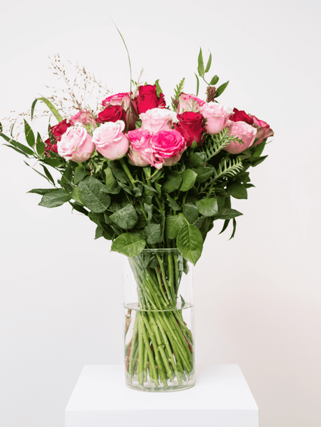 Delightful bouquet of freshly cut pink and red roses with lush greenery in a clear vase, perfect for Valentine's Day romance.