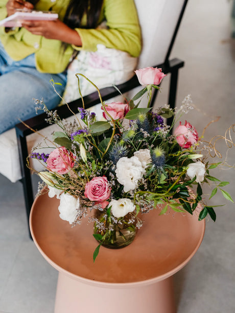 Bouquet of flowers on a small round table with a person sitting in the background.