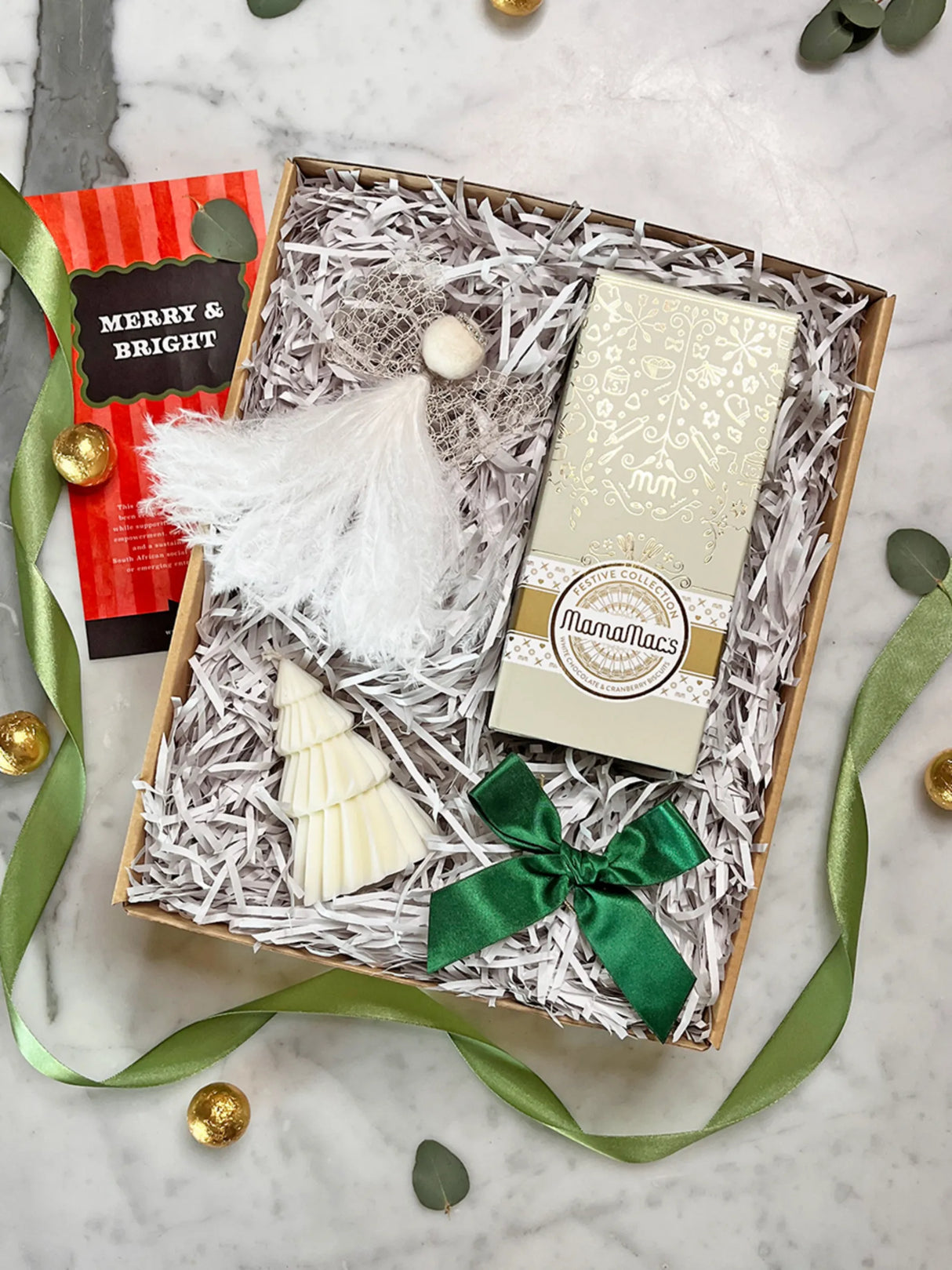 Gift box with Christmas tree ornament, green ribbon, and white card on a marble surface.