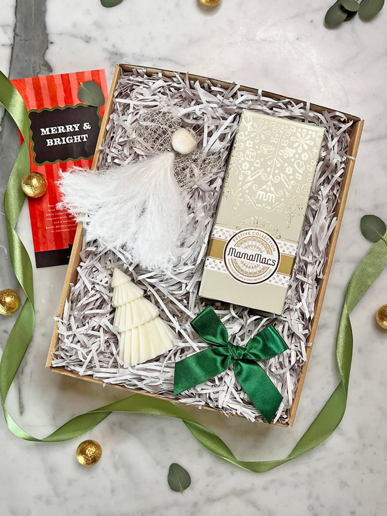 Gift box with Christmas tree ornament, green ribbon, and white card on a marble surface.