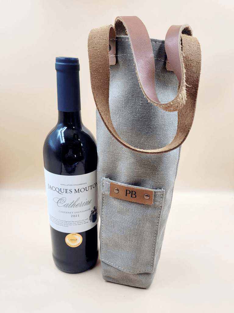 Wine bottle beside a personalised canvas wine carrier with leather straps featuring a monogrammed leather patch. 