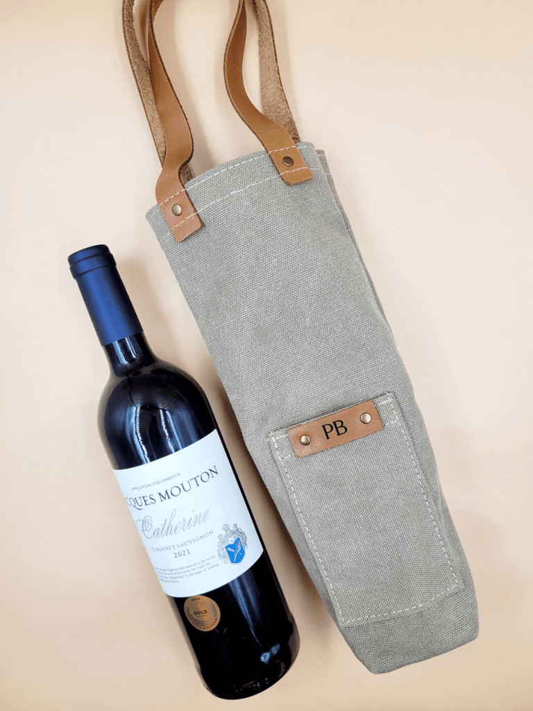 Wine bottle beside a personalised canvas wine carrier with leather straps featuring a monogrammed leather patch. 