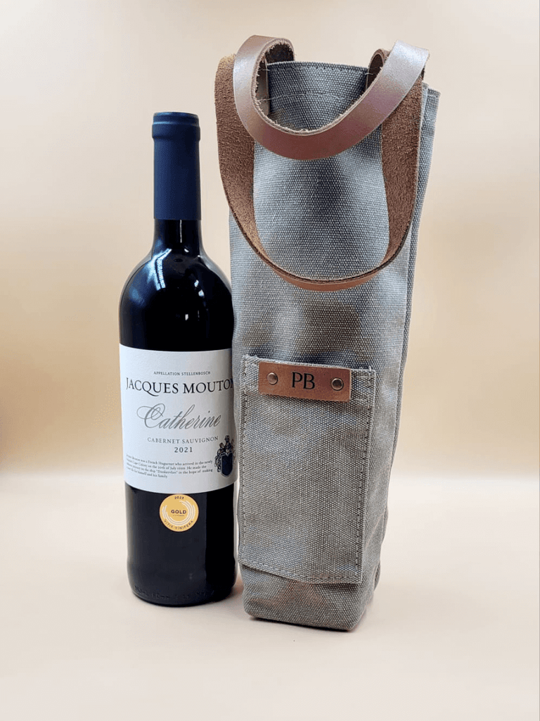 Wine bottle beside a personalised canvas wine carrier with leather straps featuring a monogrammed leather patch. 