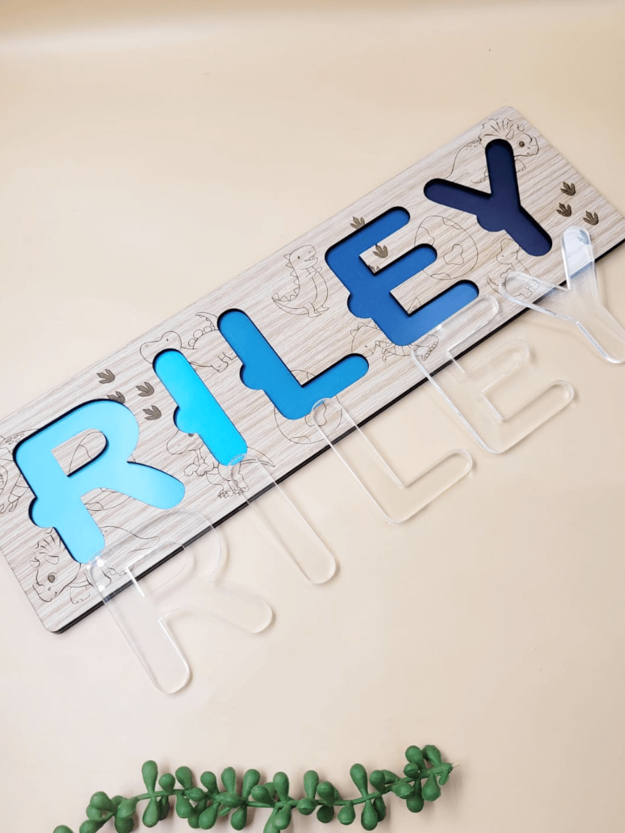 Personalized engraved name puzzle for kids with acrylic letters spelling 'Riley' on oak veneer base, dinosaur theme, top view.