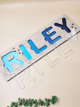 Personalized engraved name puzzle for kids with acrylic letters spelling 'Riley' on oak veneer base, dinosaur theme, top view.