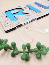 Personalised engraved name puzzle for kids with blue and clear acrylic letters on oak veneer, next to a green plant accent.